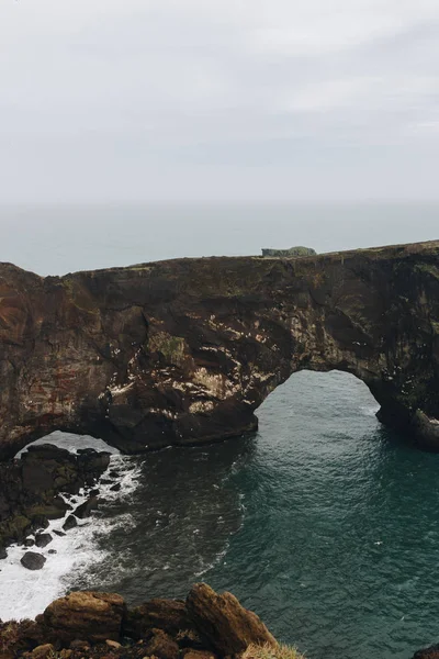 Vista panoramica di scogliera rocciosa e oceano sotto il cielo nuvoloso a Dyrholaey promontory in Vik, Islanda — Foto stock