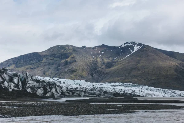 Glaciar Skaftafellsjkull y montañas nevadas contra el cielo nublado en el Parque Nacional Skaftafell en Islandia - foto de stock