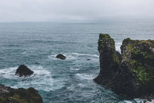 Rocky cliffs in front of blue ocean in Arnarstapi, Iceland on cloudy day — Stock Photo