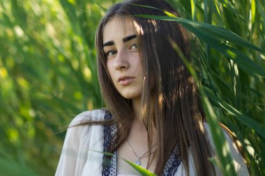 Doğal makyaj genç ve kadın ile gümüş zincir kolye boynundaki yeşil reed bulrush arka plan üzerinde.