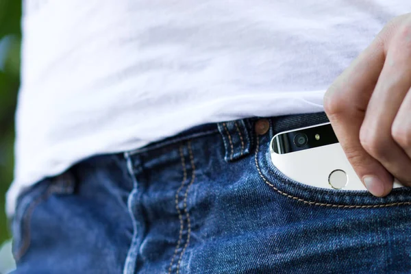 Male hand grabbing a smartphone in the left back pocket of a jeans