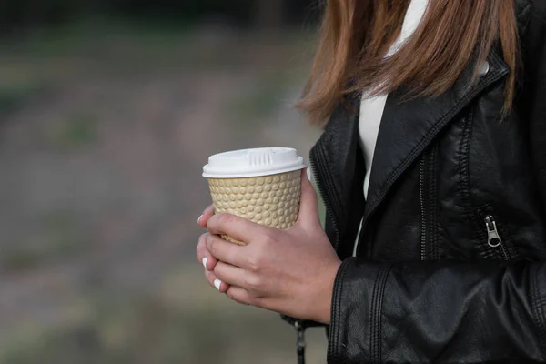 Girl with coffee cup in leather jacket in autumn park or forest. Selective focus and blur soft bokeh background.