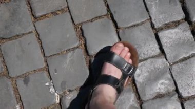 parmak arası terlikli bir adam parke taşı üzerinde yürüyor.