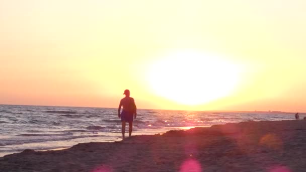 Mężczyzna spaceruje po piaszczystej plaży wzdłuż morza, ludzie szybko idą w oddali — Wideo stockowe