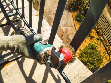 The worker uses a sander to clean the railing from paint. clipart