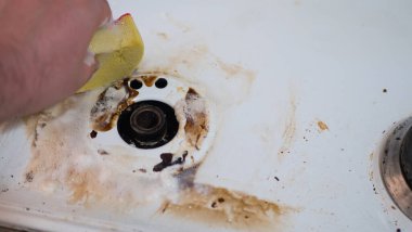 Mutfaktaki modern bir gaz sobasının yüzeyini süngerle temizleyen, duvar kiremitlerini yıkayan ve mutfak sobasını temizleyen bir adamın ellerine yakın çekim.
