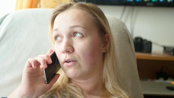 Üzgün, üzgün, depresif ve endişeli sarışın kadının dairede telefonda konuşurken yakın plan portresi.
