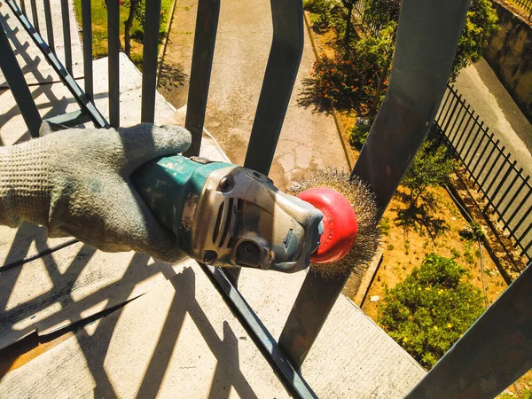 İşçi, boyadaki korkulukları temizlemek için zımpara makinesi kullanıyor..