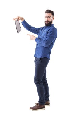 Offended young businessman holding and pointing finger at tablet computer looking at camera. Full body isolated on white background. clipart
