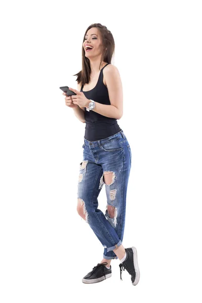相当现代的年轻女子笑着在时髦的破牛仔裤上的白色手机 在白色背景查出的充分的身体 — 图库照片
