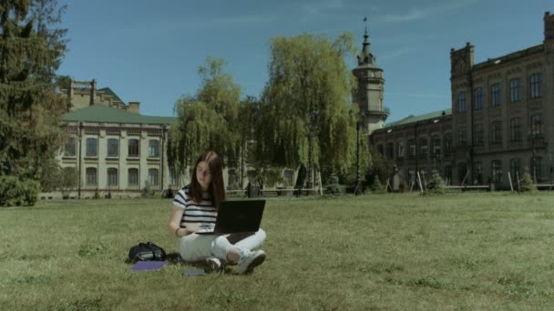 Красивая студентка работает на ноутбуке на газоне — стоковое видео