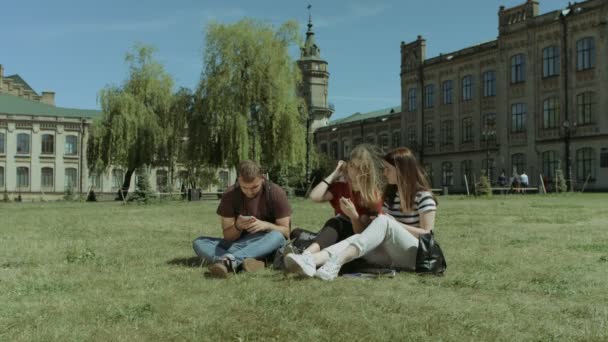 Leende studenter nätverk med smarta telefoner på gräsmatta — Stockvideo