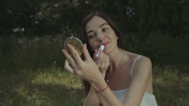 Очаровательная женщина красит губы в парке — стоковое видео