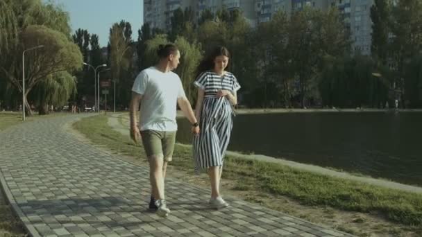 Allegro coppia incinta passeggiando lungo il lago nel parco — Video Stock