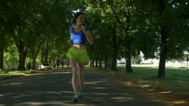 Mosolygó gyönyörű sportos nő kocogás a parkban — Stock videók
