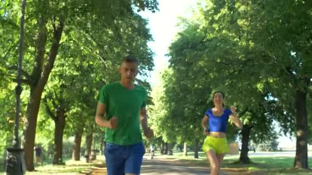 Cheerful female runner overtake man on park trail — Stock Video