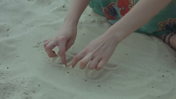 Mãos femininas desenhando rostos engraçados na areia na praia — Vídeo de Stock