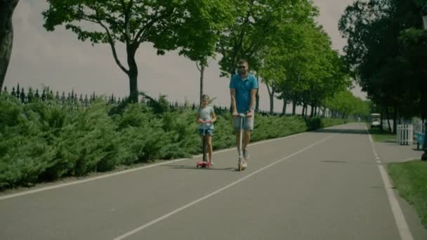 Glada far och dotter Rider skotrar i park — Stockvideo