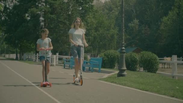 Vrolijke familie rijden kick scooters in zomer park — Stockvideo