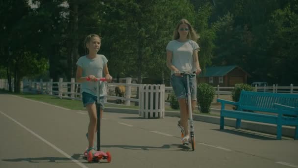 Feliz mãe e pequena filha montando scooters — Vídeo de Stock