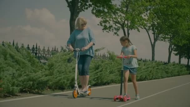 Бабушка и внучка едут на скутерах в парке — стоковое видео