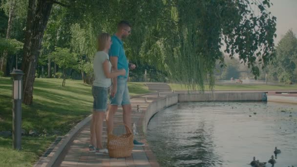 Пара миллениалов кормит уток в пруду в парке — стоковое видео