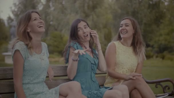 Verspielt lächelnde Frauen amüsieren sich auf Bank im Park — Stockvideo