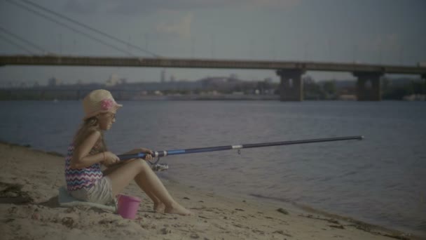 Niña con caña de pescar sentada en la orilla del río — Vídeos de Stock