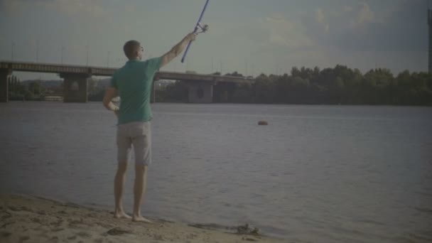 Alegre hombre milenario la captura de peces en la orilla del río — Vídeos de Stock