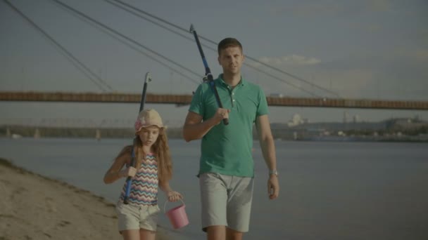 爸爸和孩子用钓鱼竿在河岸上行走 — 图库视频影像