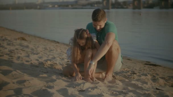 Barn och far letar snäckor i sanden på stranden — Stockvideo