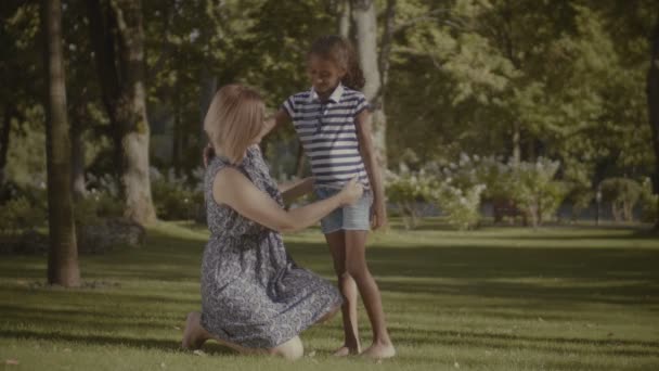 照顾白种人的母亲调整她可爱的混合种族女儿在夏季公园的衣服 而家庭在周末的休闲 爱妈妈矫直孩子的衣服户外 — 图库视频影像