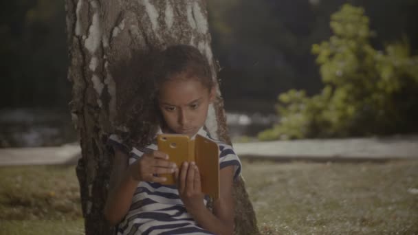 Nettes Mädchen am Handy unterm Baum — Stockvideo