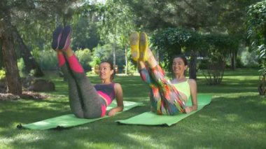 Birlikten kuvvet üst karın kasları geliştirme aktif fitness kadınlar spor giyim yaz Park, egzersiz paspaslar üzerine kaldırdı bacaklar ile ab egzersizi yapıyor. Sportif kadın mekik yapmaya açık havada egzersiz.