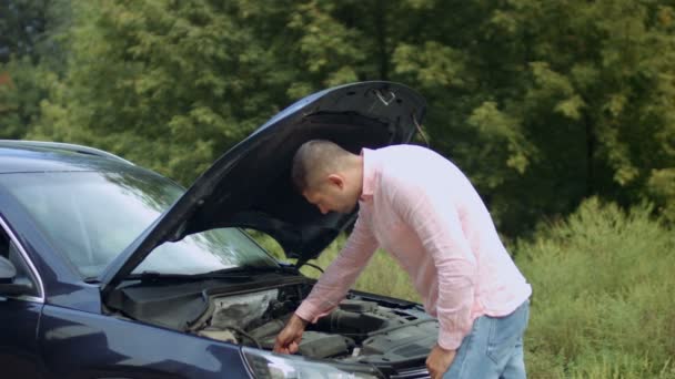 Hombre preocupado mirando debajo del capó del coche al aire libre — Vídeos de Stock
