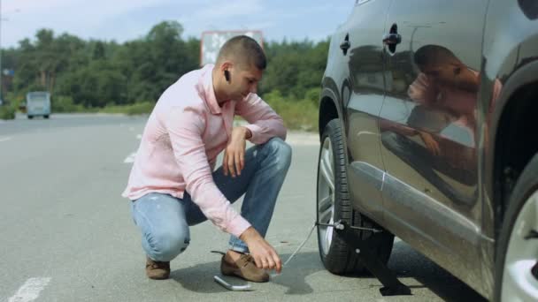 Hombre elevando coche en gato para cambiar neumático pinchado — Vídeo de stock