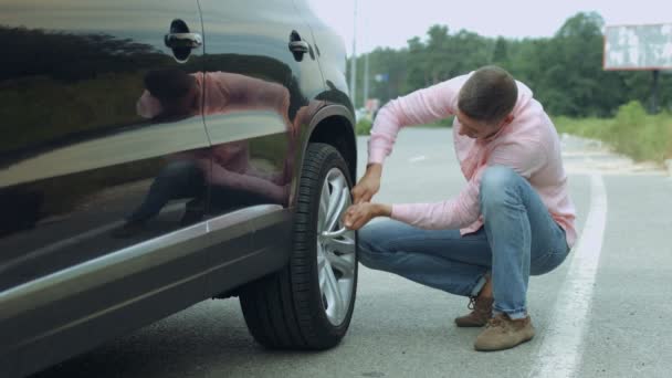 Řidič mužského pohlaví odšroubování kola automobilu klíčem, na silnici — Stock video