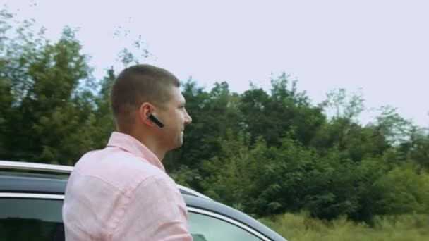 Веселый довольный мужчина, опираясь на свою машину на открытом воздухе — стоковое видео