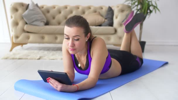 Sportlich fitte Frau mit Tablet auf Trainingsmatte liegend — Stockvideo