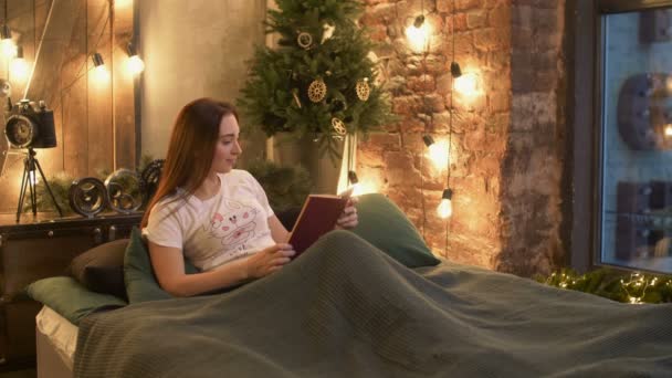 Красивая женщина в пижаме читает книгу в постели — стоковое видео
