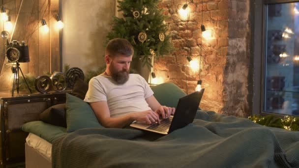 Homme indépendant couché dans son lit travaillant avec un ordinateur portable — Video