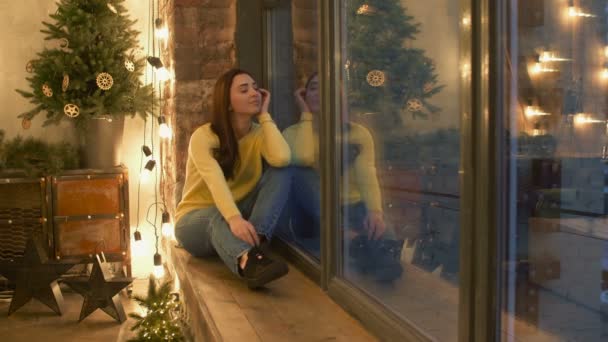 Mujer bonita soñadora mirando por la ventana por la noche — Vídeos de Stock