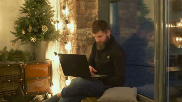 Мужчина-блоггер с ноутбуком сидит на подоконнике — стоковое видео
