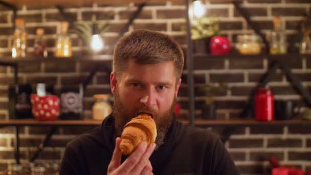 Серйозна бородата людина з жадібністю їсть круасан — стокове відео