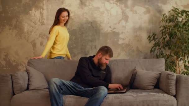 Liefdevolle vrouw omhelst drukke man die op laptop werkt — Stockvideo