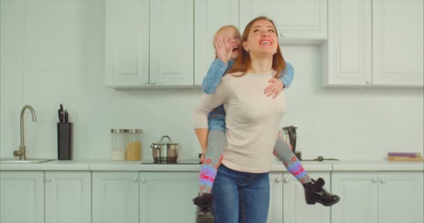 Sorglose Mutter huckepack aufgeregtes Kind in Küche — Stockvideo