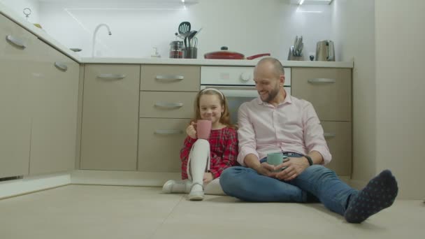 Vader en dochter ontspannen op de vloer in de keuken — Stockvideo