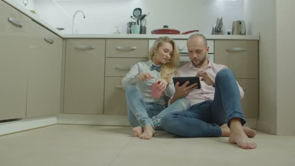 Pareja con tablet pc sentado en el suelo de la cocina — Vídeos de Stock