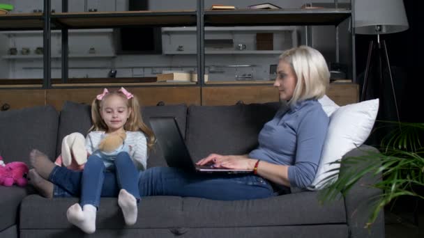 Cute girl playing toys while mom working on laptop — Stock Video