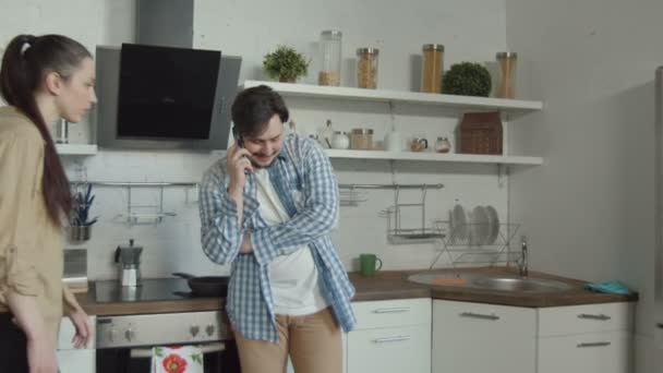 Обманщик разговаривает по смартфону на кухне — стоковое видео